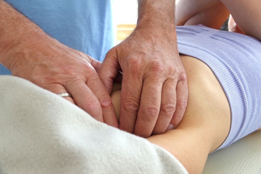 Osteopathische Behandlung: die Hände des Therapeuten am unteren Rücken einer Patientin